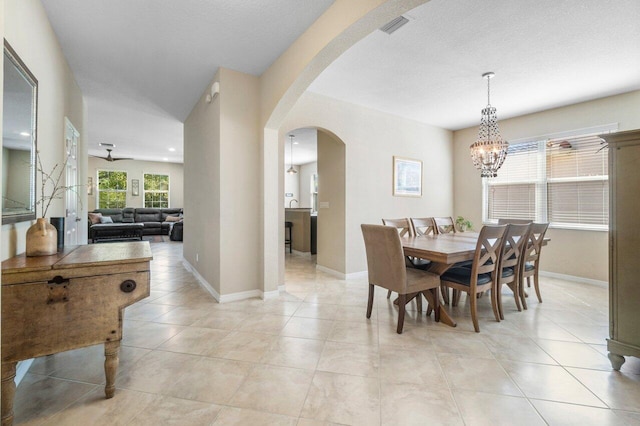 dining space featuring arched walkways, light tile patterned floors, visible vents, a textured ceiling, and baseboards