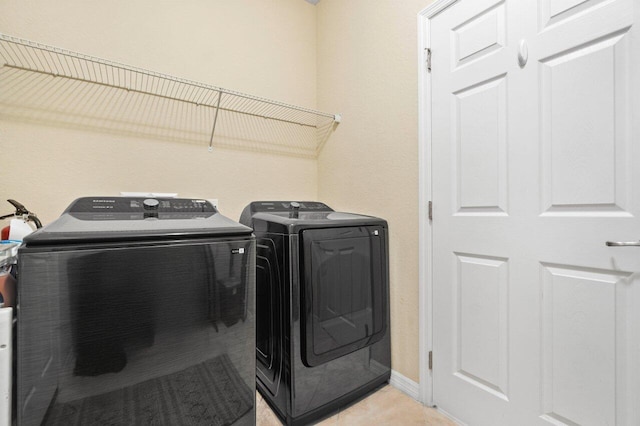 washroom featuring laundry area, washing machine and dryer, light tile patterned floors, and baseboards