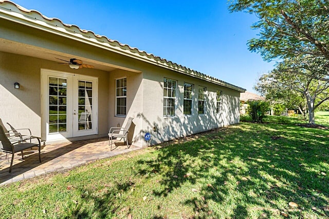 exterior space with a lawn, a ceiling fan, french doors, a patio area, and stucco siding