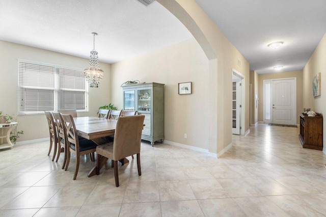 dining room with arched walkways, light tile patterned floors, a notable chandelier, and baseboards