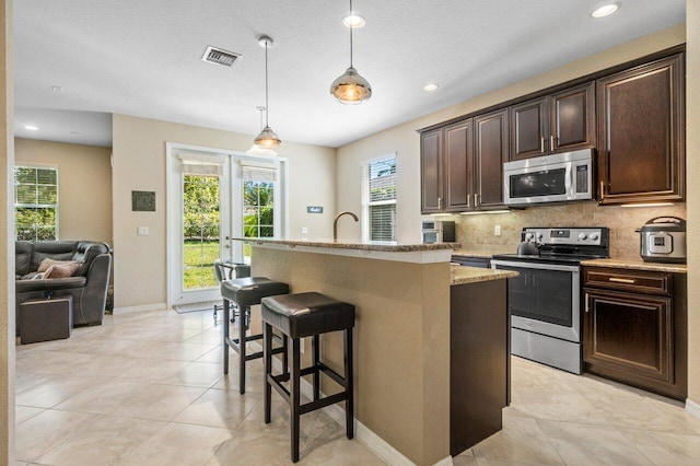 kitchen with appliances with stainless steel finishes, a healthy amount of sunlight, decorative backsplash, and a kitchen bar