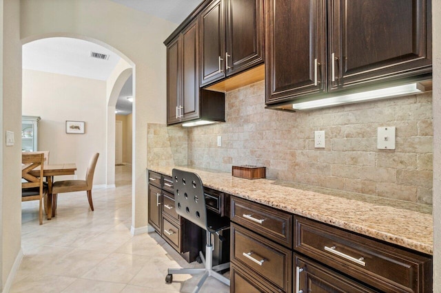 kitchen with dark brown cabinetry, visible vents, decorative backsplash, arched walkways, and light stone countertops