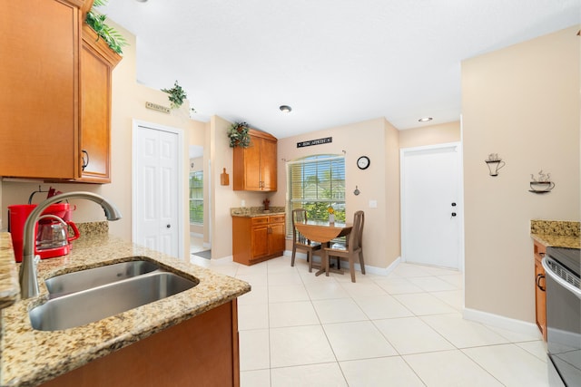 kitchen with light stone counters, light tile patterned floors, brown cabinetry, and a sink