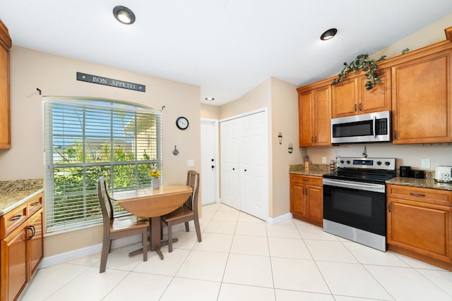 kitchen with light tile patterned floors, stainless steel appliances, brown cabinets, and light stone countertops