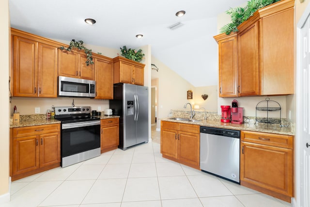 kitchen featuring brown cabinetry, visible vents, light stone countertops, a sink, and stainless steel appliances