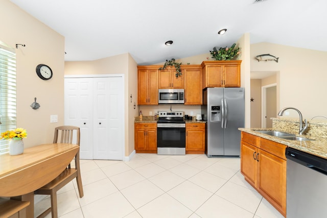 kitchen featuring light stone countertops, lofted ceiling, a sink, stainless steel appliances, and brown cabinets