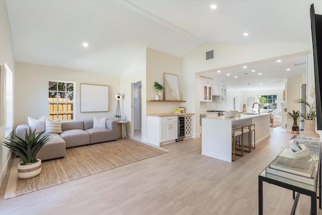living room with wine cooler, light wood-style floors, high vaulted ceiling, and recessed lighting