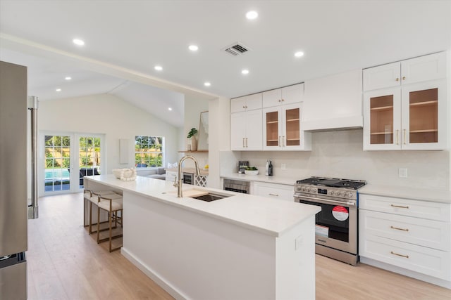 kitchen with appliances with stainless steel finishes, a sink, light wood-style floors, vaulted ceiling, and white cabinets