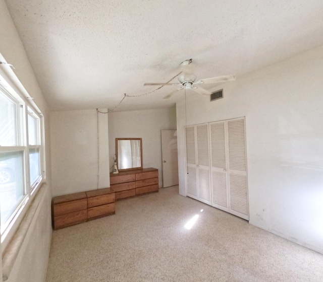 unfurnished bedroom featuring visible vents, ceiling fan, vaulted ceiling, a textured ceiling, and a closet