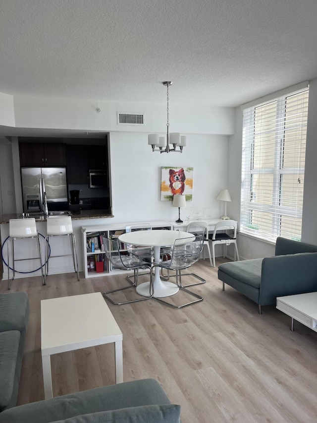 living area with a textured ceiling, light wood-style flooring, visible vents, and a notable chandelier