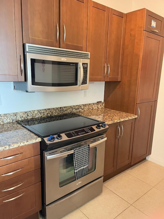 kitchen with brown cabinetry, light stone counters, stainless steel appliances, and light tile patterned flooring