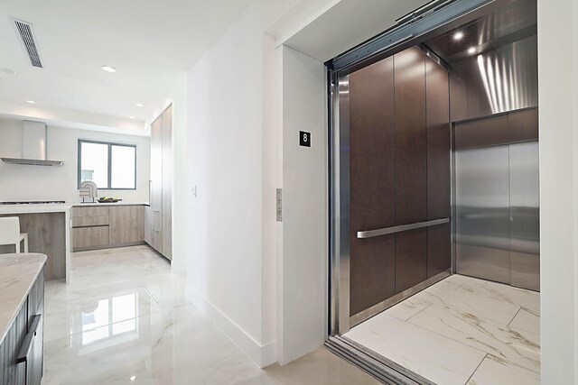 interior space with visible vents, modern cabinets, marble finish floor, elevator, and wall chimney exhaust hood