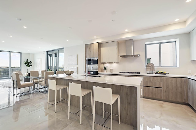 kitchen with a breakfast bar, light countertops, wall chimney exhaust hood, and modern cabinets