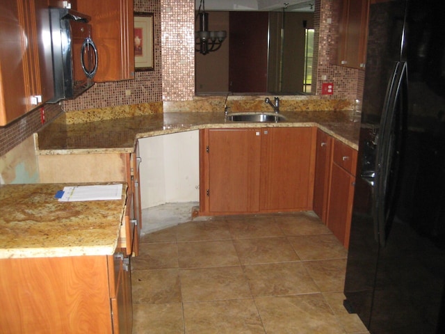 kitchen featuring a sink, brown cabinets, backsplash, and black fridge