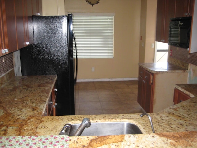 kitchen with light stone counters, decorative backsplash, tile patterned floors, and freestanding refrigerator