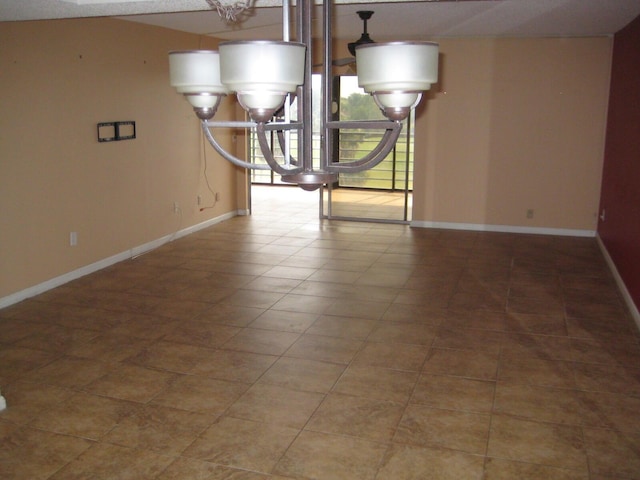 tiled spare room featuring a notable chandelier and baseboards