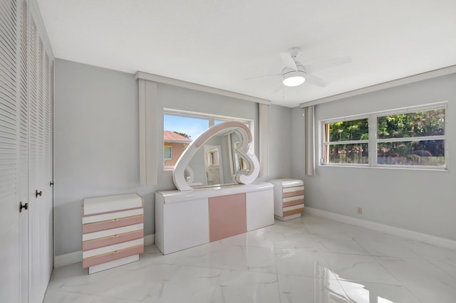 unfurnished bedroom featuring marble finish floor, multiple windows, a ceiling fan, and baseboards