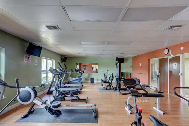 exercise room with a drop ceiling, wood finished floors, and visible vents