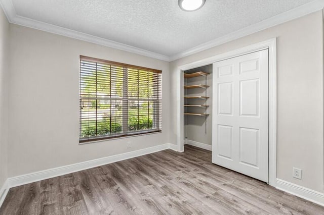 unfurnished bedroom with baseboards, ornamental molding, wood finished floors, a closet, and a textured ceiling