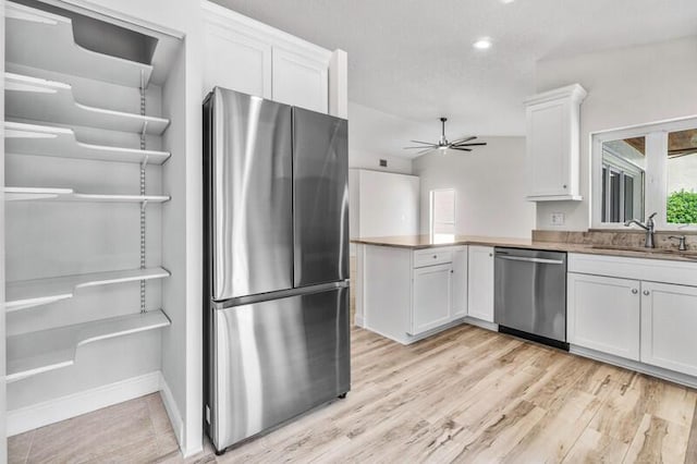 kitchen featuring light wood-type flooring, white cabinets, stainless steel appliances, a ceiling fan, and a sink