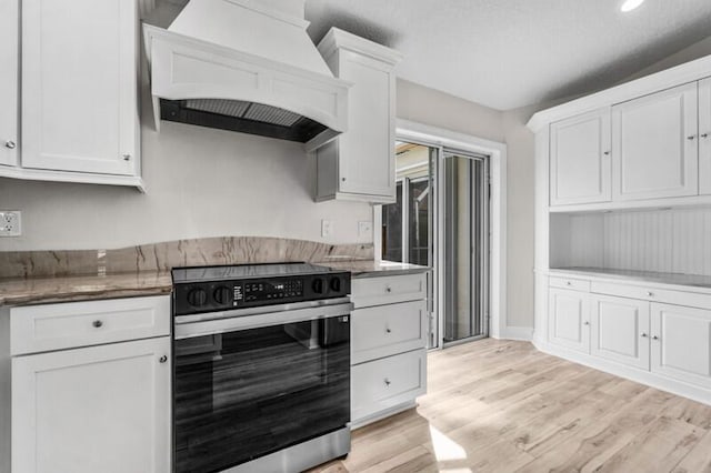 kitchen featuring custom exhaust hood, white cabinets, light wood-type flooring, and electric range oven