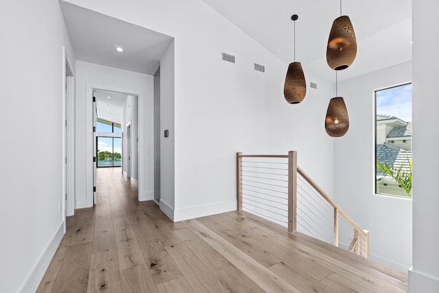 hall with a wealth of natural light, light wood-type flooring, visible vents, and an upstairs landing