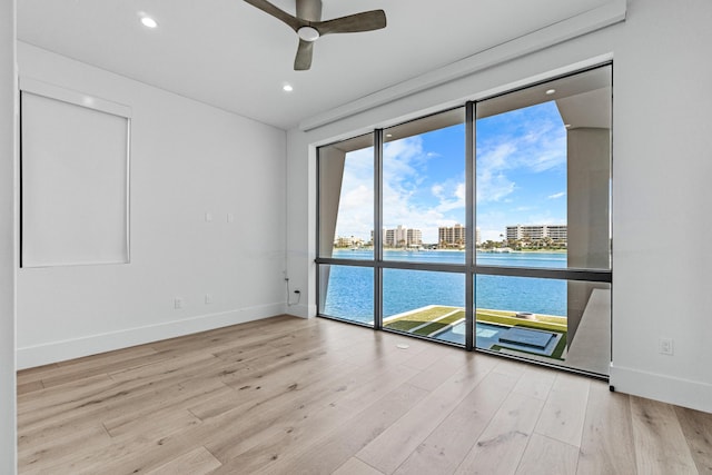 spare room featuring recessed lighting, a water view, a ceiling fan, wood finished floors, and baseboards