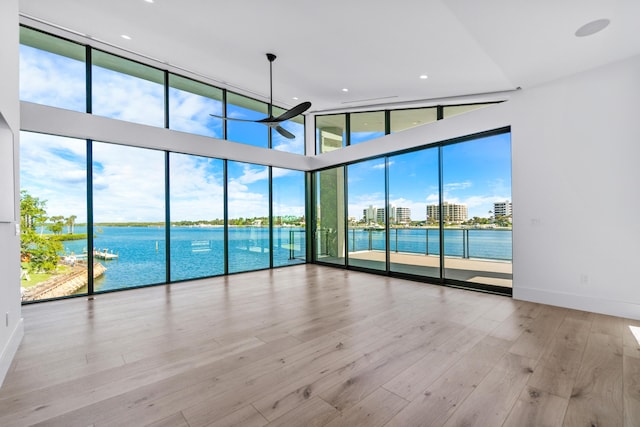 unfurnished room with baseboards, ceiling fan, wood finished floors, a water view, and a wall of windows