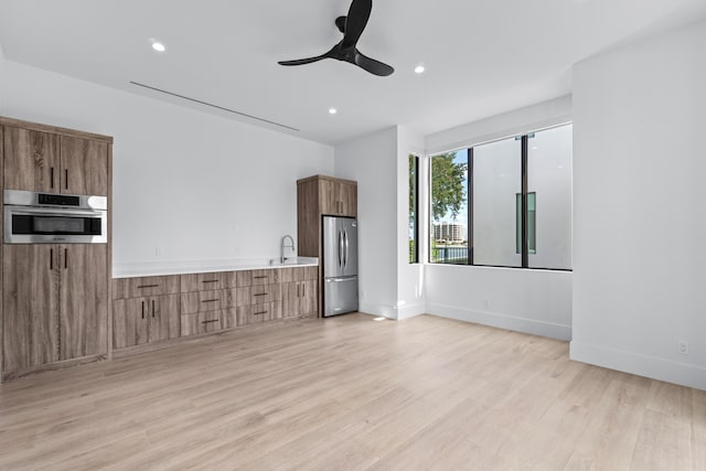 unfurnished living room featuring light wood finished floors, recessed lighting, a ceiling fan, a sink, and baseboards