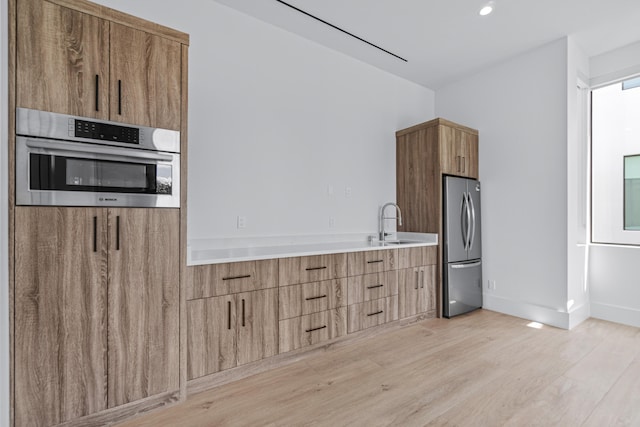 kitchen featuring appliances with stainless steel finishes, modern cabinets, a sink, and light wood-style flooring