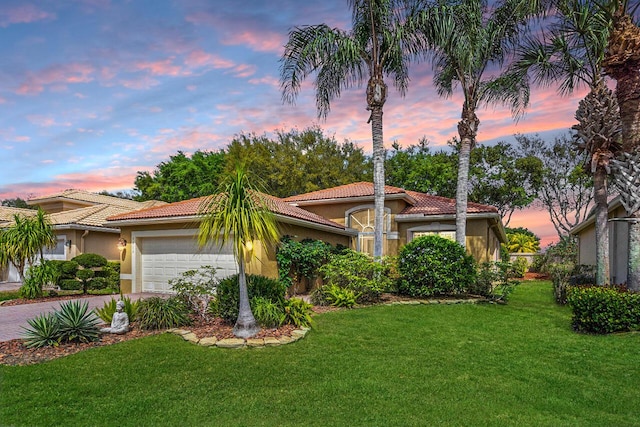 mediterranean / spanish-style house with a front yard, driveway, stucco siding, a garage, and a tile roof