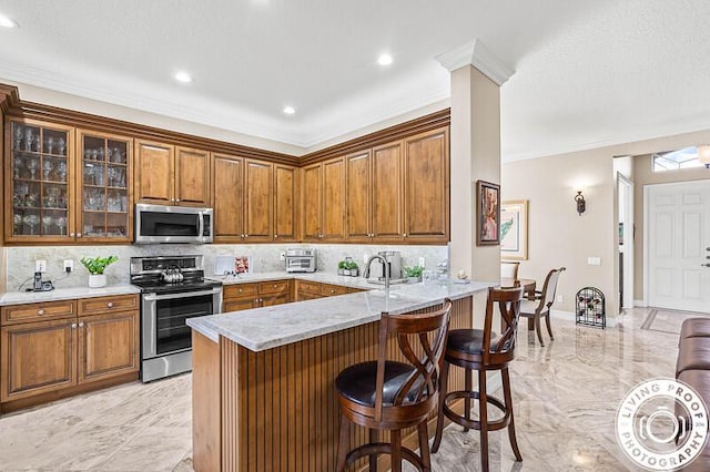 kitchen featuring backsplash, a breakfast bar, brown cabinets, appliances with stainless steel finishes, and marble finish floor