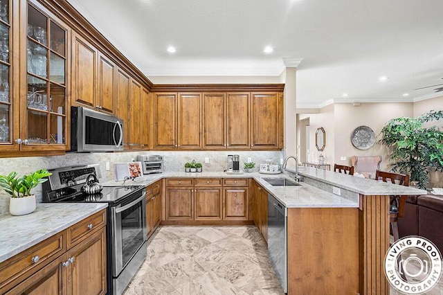 kitchen featuring a breakfast bar, a peninsula, brown cabinetry, stainless steel appliances, and a sink