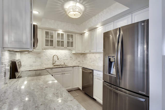 kitchen with light stone countertops, decorative backsplash, stainless steel appliances, white cabinetry, and a sink