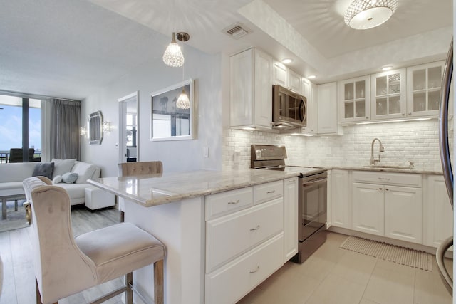 kitchen featuring visible vents, appliances with stainless steel finishes, a peninsula, white cabinets, and a sink