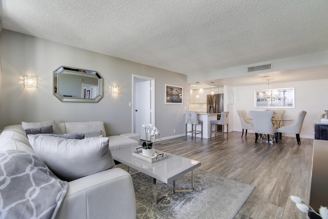 living room featuring visible vents, baseboards, light wood-style flooring, a notable chandelier, and a textured ceiling