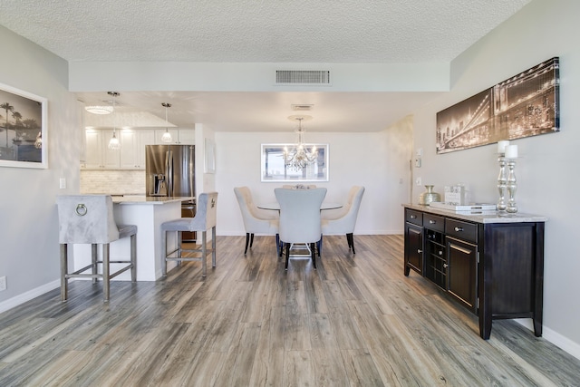 dining space with visible vents, baseboards, a textured ceiling, and wood finished floors