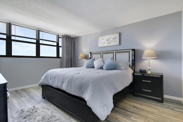 bedroom featuring light wood finished floors, a textured ceiling, and baseboards