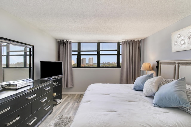 bedroom featuring light wood-style flooring, a textured ceiling, and baseboards