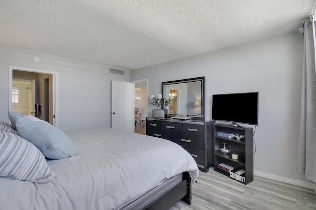 bedroom with visible vents, baseboards, light wood-style floors, and a textured ceiling