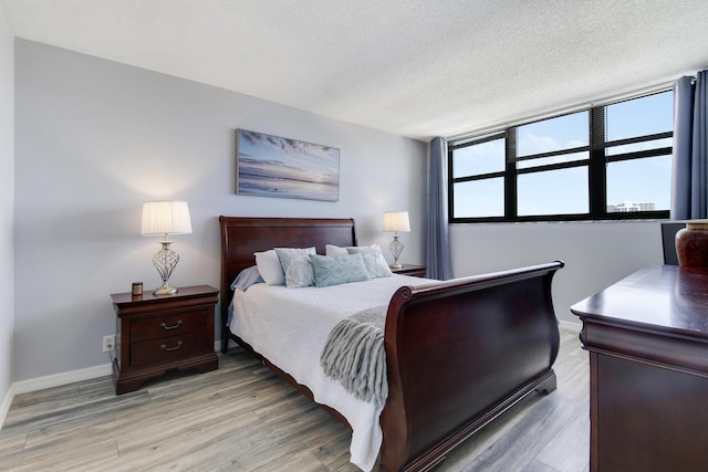 bedroom with baseboards, a textured ceiling, and light wood finished floors