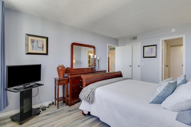 bedroom featuring visible vents, baseboards, light wood-style floors, a closet, and a textured ceiling