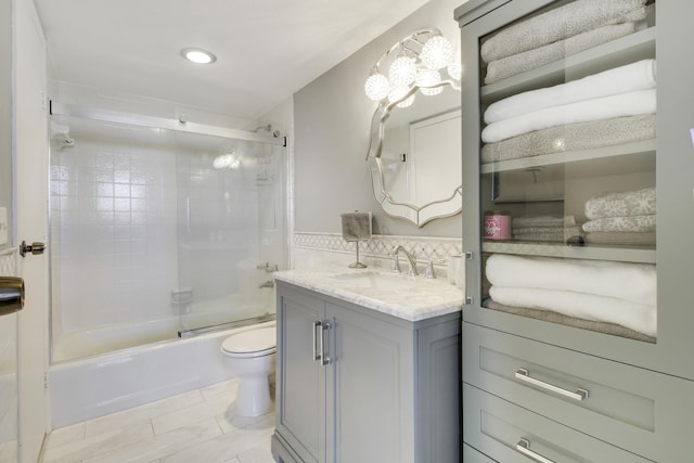 bathroom with combined bath / shower with glass door, toilet, and vanity