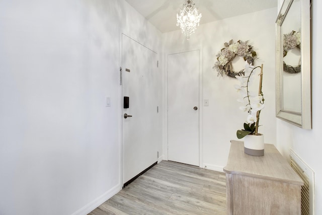 entryway with light wood-style flooring, a notable chandelier, and baseboards