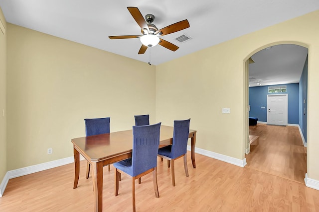 dining room with arched walkways, light wood finished floors, visible vents, and baseboards