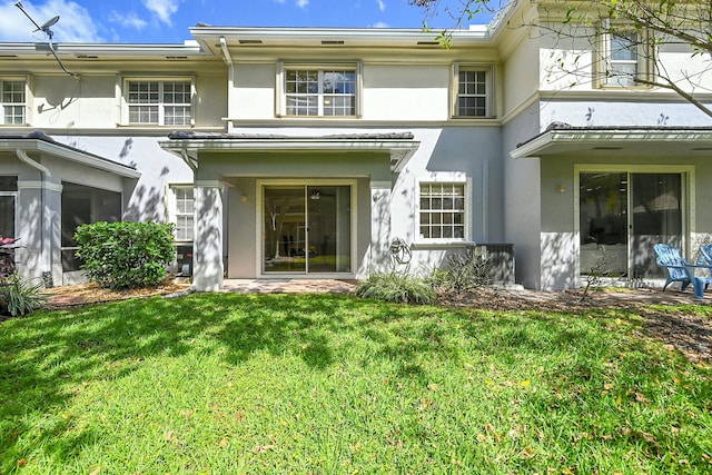 rear view of house featuring a lawn and stucco siding