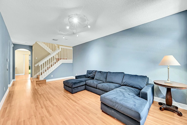 living room with arched walkways, stairway, a textured ceiling, wood finished floors, and baseboards