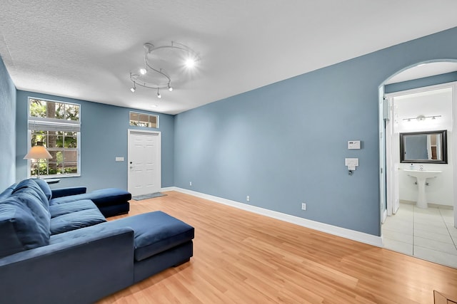 living area with arched walkways, rail lighting, a textured ceiling, light wood-type flooring, and baseboards