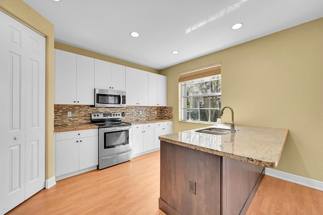 kitchen with a peninsula, a sink, appliances with stainless steel finishes, light wood finished floors, and tasteful backsplash