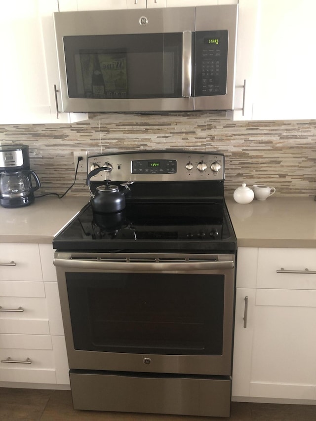 kitchen with stainless steel appliances, light countertops, white cabinetry, and backsplash